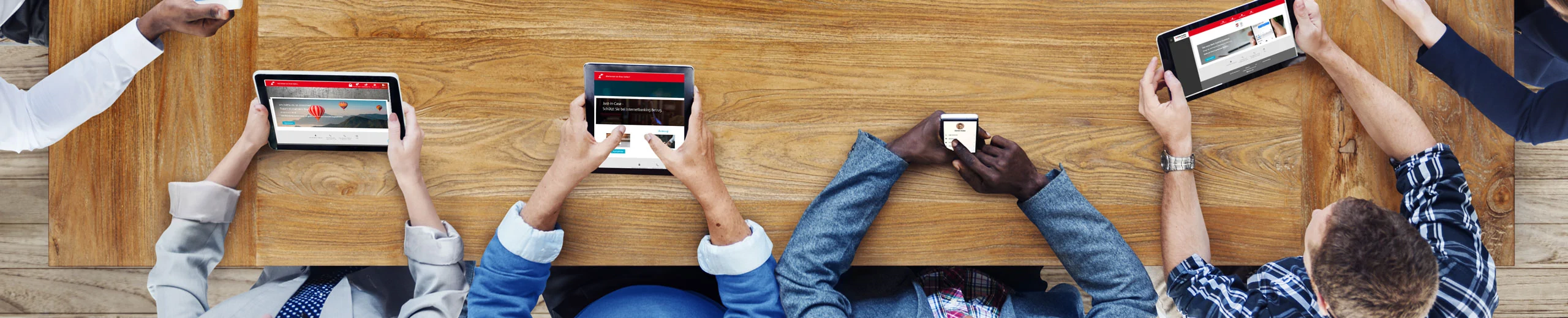 Eine Gruppe von Menschen sitzen um einen Tisch herum und schauen auf ihr Tablet oder Smartphone