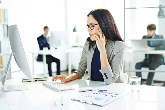 Junge Frau sitzt an ihrem Schreibtisch und telefoniert