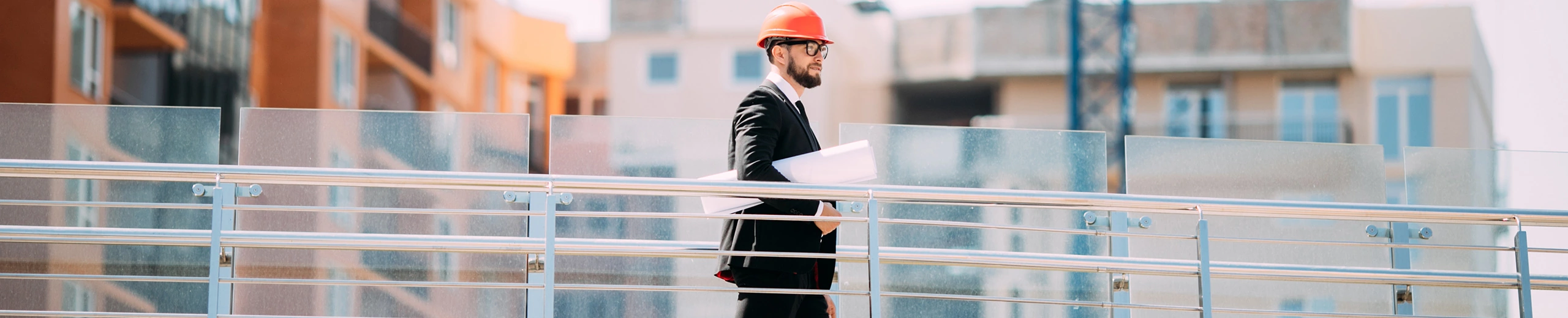 Ein Mann im Anzug und mit Bauhelm geht mit einem Plan unter dem Arm auf einer Großbaustelle