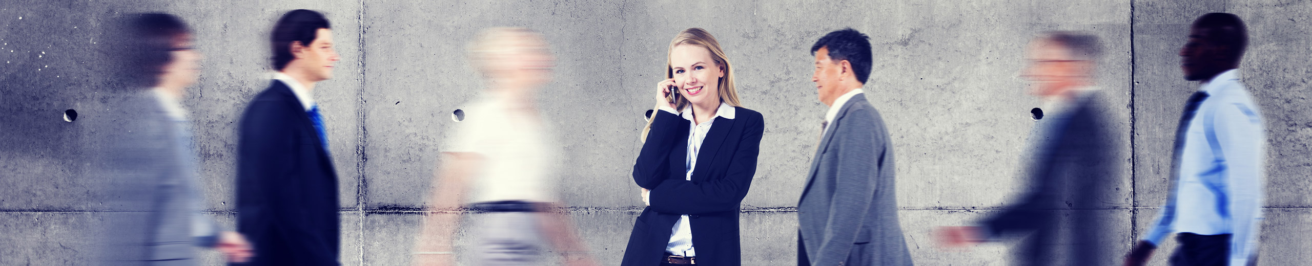 Im Vordergrund telefoniert eine Geschäftsfrau; im Hintergrund gehen Männer