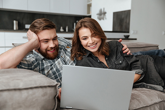 A woman and a man together on a couch in front of a laptop