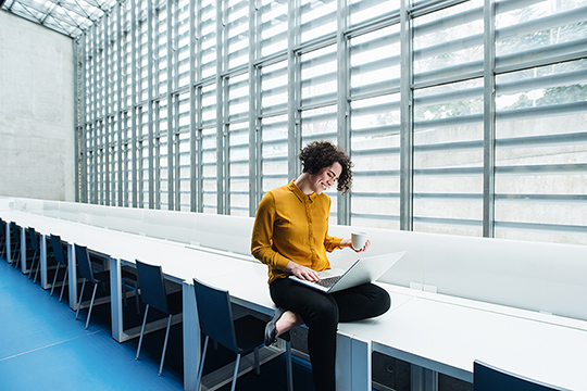 Woman wearing a yellow blouse looks at her laptop