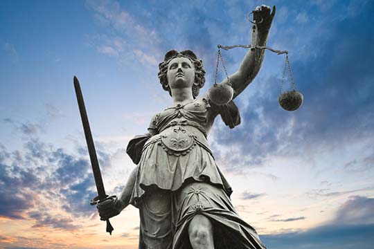 Justizstatue mit Schwert und Waage in der Hand vor dem bewölkten Himmel