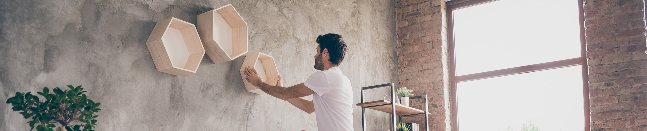Mann steht auf einer Leiter im Wohnzimmer und montiert Holzboxen an der Wand