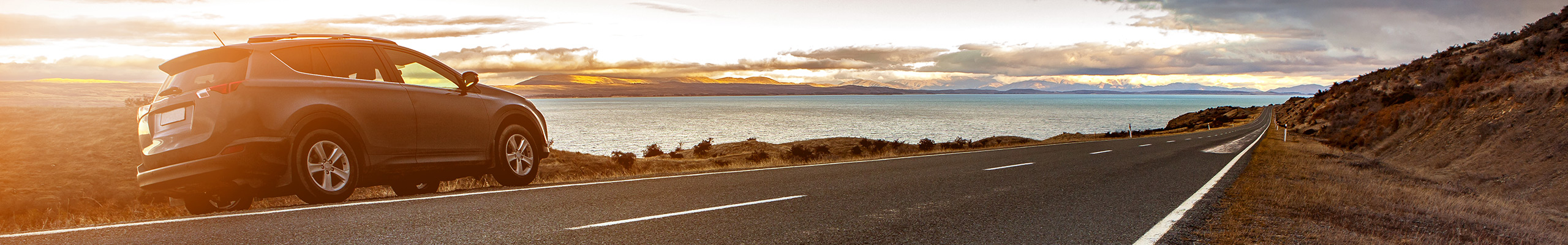 Ein Auto steht am Straßenrand vor dem Meer im Sonnenuntergang