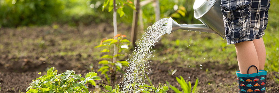 Ein Kind in Gummistiefeln gießt den Garten