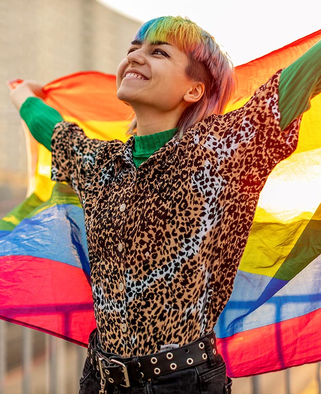 Eine junge Frau mit bunten Haaren hält eine Regenbogenfahne in die Höhe
